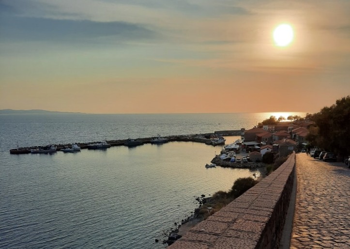 Stoned promenade by the sea, with a small port on the background and then sun a little before sunset