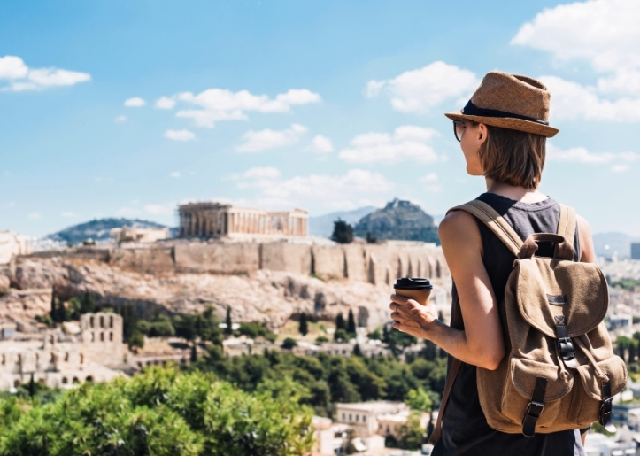 Woman with a cup of coffee and a backpack gazing at the acropolis hill