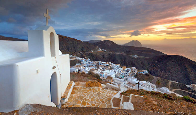 Small white church on top of picturesque settlement in the background dark hills at sunset.