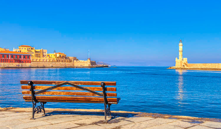 Bench with sea view. On one side traditional colored buildings and stone walls and on the other a stone lighthouse.