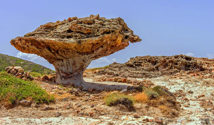 Mushroom-shaped rock in a rocky landscape with low green vegetation. 