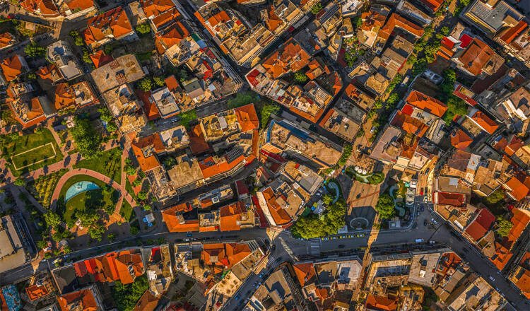Aerial view of a dense urban area with red-roofed buildings, winding streets, and green spaces in a lively cityscape.