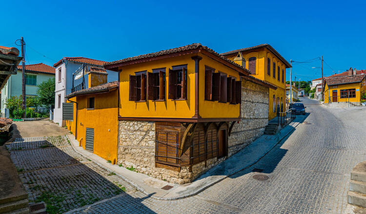 Traditional stone low building with yellow surfaces and wooden windows at the intersection of paved streets. Sunshine.