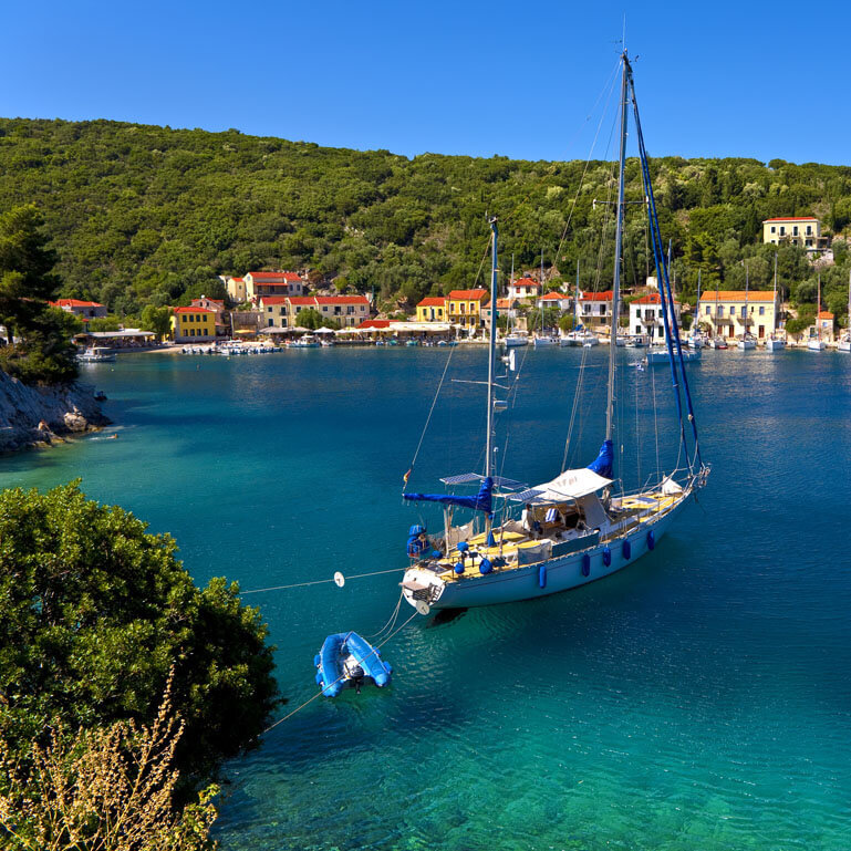 Seaside village with a lot of pine tree and a sailing boat anchored near the port