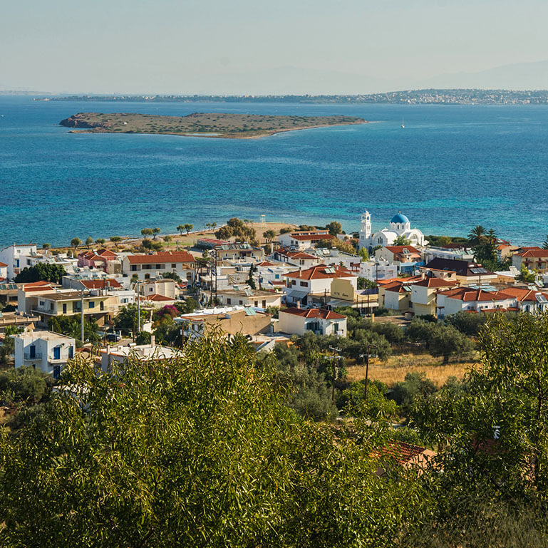 Seaside village with tiled rooftops, a white washed church with a blue dome and an islet in the background