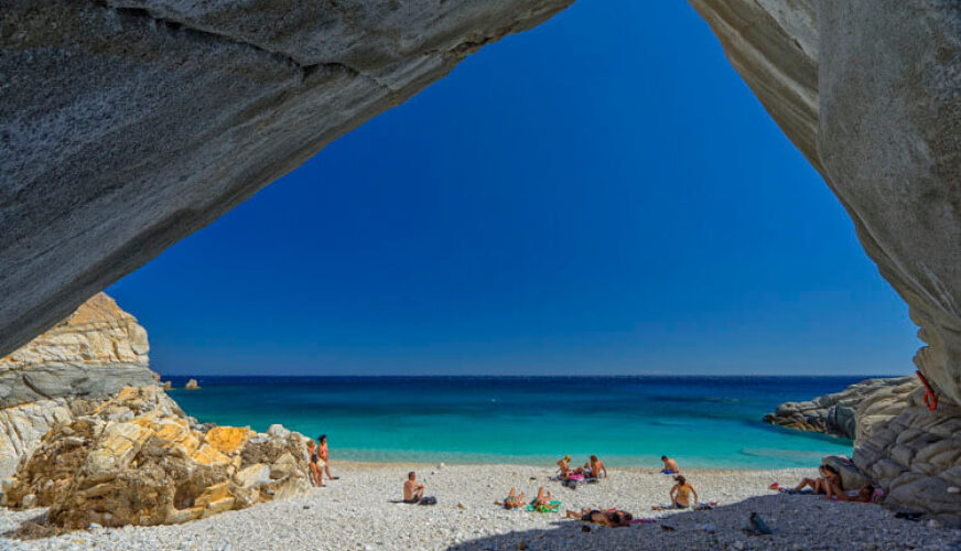 Beach with white stones and turquoise waters. People in swimsuits on the beach. Rocks around like a cave. 