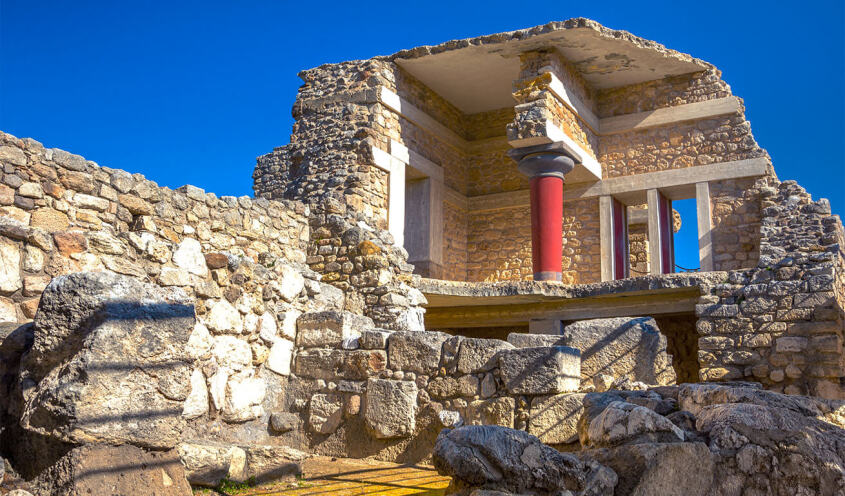 Part of an ancient stone-built 2-storey building with a red column and openings. The interior of the upper floor and parts of walls can be seen.