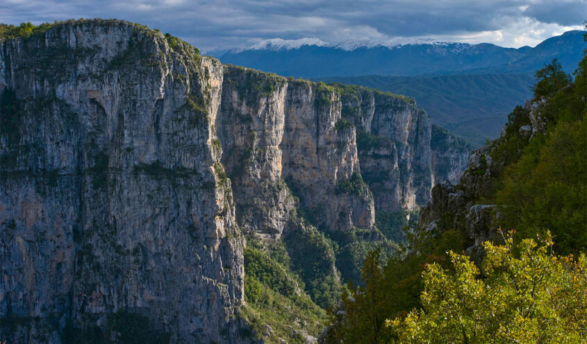 Φαράγγι με ψηλά απόκρημνα βράχια και πυκνή βλάστηση τριγύρω. Συννεφιά με ήλιο.