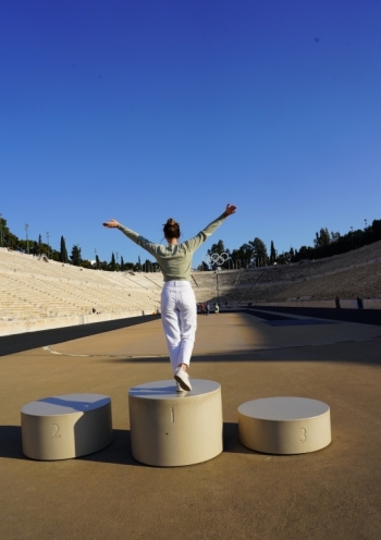 a girl tourist standing with her back and arms open in the air, in front of the panathenaic stadium  