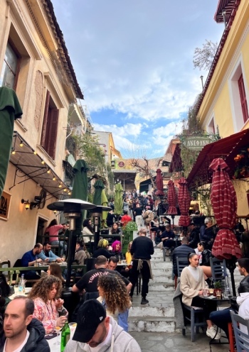 view of a small street in Plaka, Athens, with small steps with tables where people sit and enjoy their drinks/food