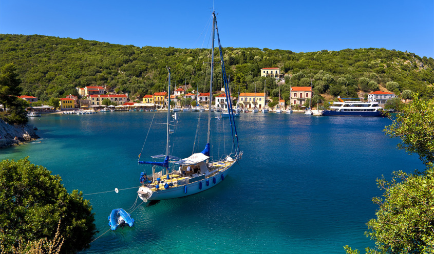 sailing boat in deep blue sea and a small houses in the background