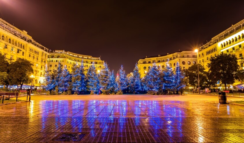 Christmas trees in a big square surrounded by building at night time